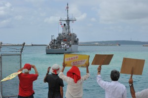 出港する米海軍掃海艦にプラカードを持って抗議をする抗議団のメンバーら＝24日、平良港
