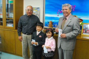 下地市長（左）が新入学児童代表の２人にグッズを贈った＝４日、市役所平良庁舎