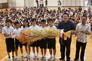 全校児童で折った鶴３０００羽をＪＣに手渡す児童会の皆さん＝11日、平良第一小学校体育館