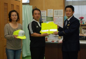 宮城所長（右）から与那覇会長にベストが手渡された＝11日、久松小学校