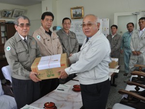 安村社長（左）に飲料水を贈り激励する下地市長＝22日、宮古製糖城辺工場
