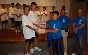 宮古島夏まつりで集めた募金を砂川バットマンのメンバー（写真右）が宮古市少年野球選抜チームに寄贈した＝３日、ホテル共和