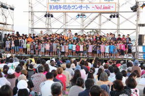 デビュー10周年記念コンサートの舞台で「ボクは国王」を歌う勇さんと小学生たち＝10月20日、久松漁港内多目的広場