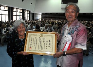 仲井真知事（右）から健康長寿１００歳表彰を受けて笑顔の仲田ウメさん＝12日、城辺公民館