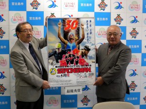 第３０回大会の公式ポスターに選ばれた高野昭さんの作品を発表する下地市長（右）と長濱副市長＝２０日、市役所平良庁舎