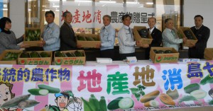 新城本部長（右から４人目）らから地元産の野菜が川満弘志市教育長（同３人目）らに贈呈された＝１０日、ＪＡあたらす市場前
