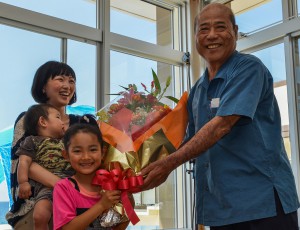 豊見山会長（右）から来園者20万人目の下地茶花さんと家族に花束などが贈られた＝１２日、海中公園