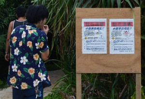 観光客らは宮古島署が設置した注意喚起の看板を注意深く読んでいた＝１５日、砂山ビーチ入口