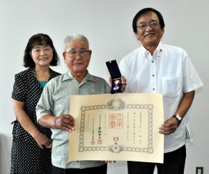 市議会の真栄城徳彦議長（右）から高齢者叙勲の伝達を受けた砂川松吉さん（中央）。左は三女の上地久子さん＝２日、市役所平良庁舎