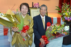 孫たちから贈呈された花束を手にする仲間克氏（右）と妻の由美子さん＝１３日、城辺公民館