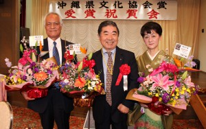 祝いの花が贈られた（左から）粟國さん、砂川会長、池田さん＝１６日夜、市平良西里のホテル