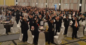 敬老会で伊良部大橋の実現を祝し万歳三唱する郷友ら＝２２日、宜野湾市内のホテル