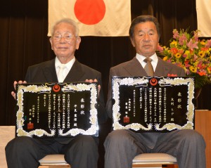 県文化功労者として表彰された平良さん（左）と友利さん代理の息子・孝雄さん＝２６日、県庁講堂