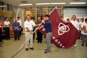 選手団の代表に団旗を手渡す長濱博文会長（左）。総合８位以内に期待を込めた＝５日、市役所平良庁舎