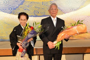 受賞を祝い花束の贈呈を受けた平良重信さん（右）夫妻＝２０日、市内ホテル