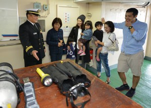 潜水支援室で機器の説明を受ける見学者。左は川崎船長＝３０日、水中処分母船６号船上