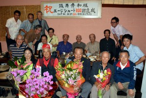 関係者が集い、阪井さん（前列左から２人目）のエージシュート１００回の偉業達成を祝った＝市内飲食店
