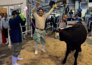 県内最高額を付けた牛を生産した上地さん（中央）。踊って喜びを表現した＝１９日、ＪＡおきなわ宮古家畜市場