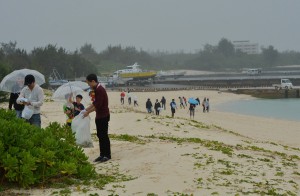 雨の中、傘をさしてごみを拾う参加者ら＝２５日、与那覇前浜ビーチ