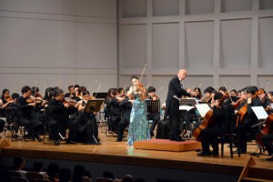 バイオリン演奏で聴衆を魅了するサラ・チャンさん（中央）。指揮は天野誠さん＝６月２９日、マティダ市民劇場