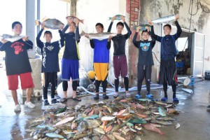 大物の魚を持ち上げて記念撮影する生徒たち＝２６日、狩俣漁港