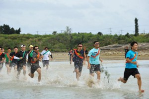 潮が満ち始めた干潟で力走する水中駅伝の参加者ら＝６日、与那覇サニツ浜
