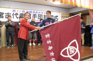 平良選手（手前右）に団旗を手渡す長濱会長（同左）＝４日、平良西里のホール