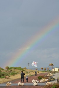 色鮮やかな虹をバックに凧揚げを楽しむ参加者ら＝１４日、平良のトゥリバー地区