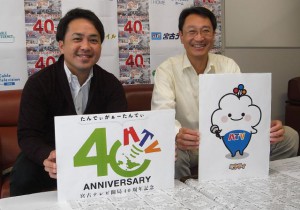 オリジナルキャラクター「ミヤティ」を持つ大窪部長（右）と、記念ロゴマークを持つ総務部の友利恵之さん＝１８日、宮古テレビ