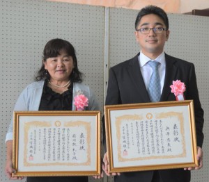 県母子保健大会で表彰された荷川取さん（左）と、奥平さんの代理で出席した息子の忠寛さん＝１８日、宜野湾市民会館