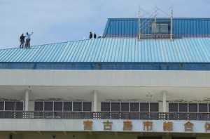 屋根の上では初日から複数の作業員が急ピッチで作業を進めていた＝11日、市総合体育館