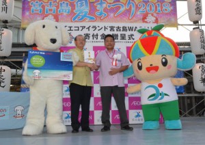 マックスバリュ先島運営部長の大城さん（中央右）から長濱副市長に寄付金が贈呈された＝21日、下里公設市場前の特設ステージ