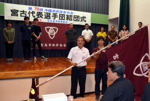 市体育協会の長濱博文会長（左）から選手団で卓球の伊志嶺圭司さんに団旗が手渡された＝９日、富名腰公民館