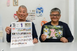 笑顔カレンダーの完成、発売を発表する藤井理事（左）と下地会長＝７日、市内の印刷会社