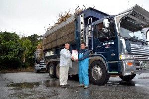 30年間サトウキビ運搬一番乗りを続ける平良栄喜さん（右）。沖縄製糖から記念品を受けた＝17日、沖縄製糖宮古工場
