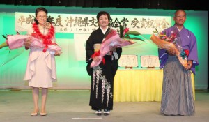 受賞を祝う花束を受け取った（左から）中松代表、池間さん、松堂さん＝19日、市内ホテル