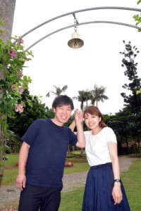 ２本のヤシの木に架けたアーチの下、幸せの鐘を鳴らす倉谷龍一さん（左）と妻の梓さん＝30日、市熱帯植物園