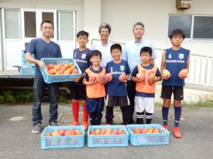 田上さん（左）からマンゴーを受け取る児童ら＝16日、上野小学校
