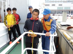 ロープの結び方を学び海保の職員と一緒になって結ぶ参加者たち＝10日、平良港に係留されている巡視船「はりみず」