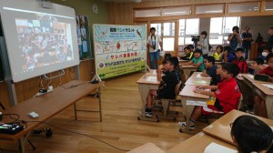 栃木県市貝町の小貝小児童とモニターを通して交流する伊良部島小の児童たち＝16日、伊良部島小学校