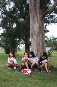 仲間たちと木陰に座って俳句を詠む子どもたち＝15日、カママ嶺公園