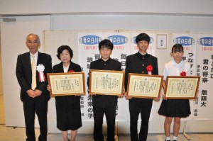 宮國教育長（左）から表彰状が授与された（左から２人目から）新城さん、砂川さん、洲鎌さん、松堂さん＝16日、市未来創造センター多目的ホール
