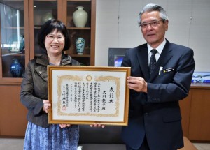 大川さん（左）に座喜味市長から表彰状が伝達された＝26日、市役所