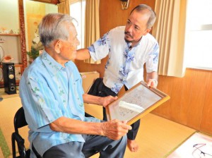仲間会長（右）から佐渡山さんに米寿の表彰状が手渡されたほか、自治会役員が高齢者宅を１軒１軒訪ねて長寿を祝福した＝20日、池間島