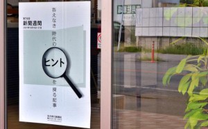 本社の入り口にあるガラス戸には新聞週間のポスターが掲示され、その横には市議選のポスター掲示板が反射して映る
